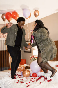 Couple jumping on bed with champagne after proposal in hotel