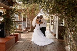 Bride and groom dancing under a large tree on a wood platform during first dance