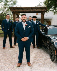 Groom and groomsmen with car in front of venue