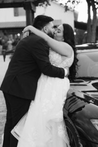 Bride and groom kissing against car in front of Waco venue