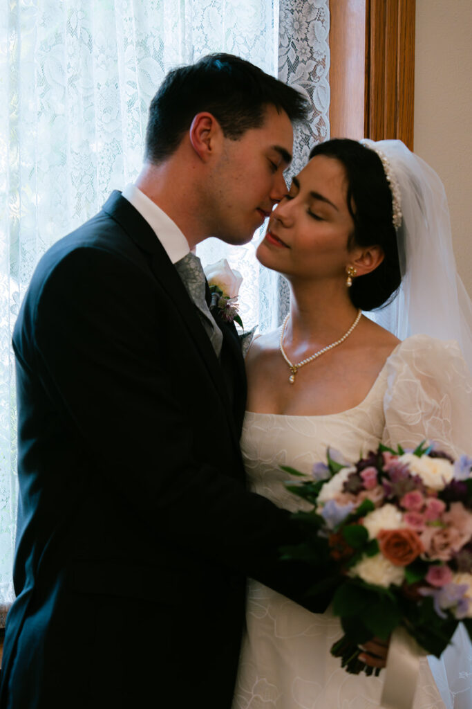 Bride and groom against window during bridal portraits after Catholic wedding